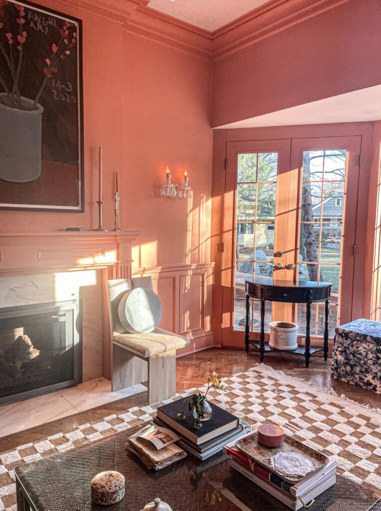 Peach living room with fireplace, French doors, artwork, and checkered rug in the morning light.